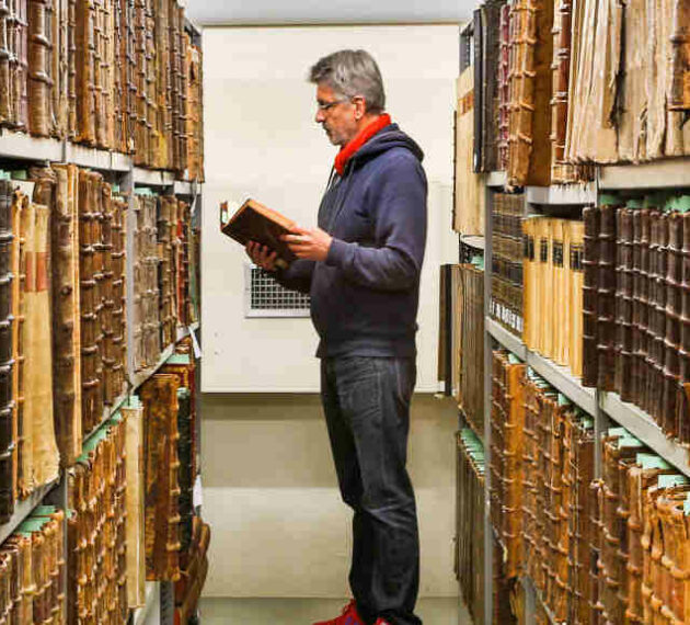 Header homme feuilletant un livre dans une bibliothèque de livres anciens