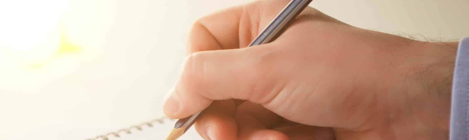 Une main d'homme avec un crayon qui écrit sur un bloc note