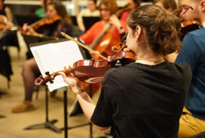 Jeune fille de dos qui joue du violon face à un pupitre.