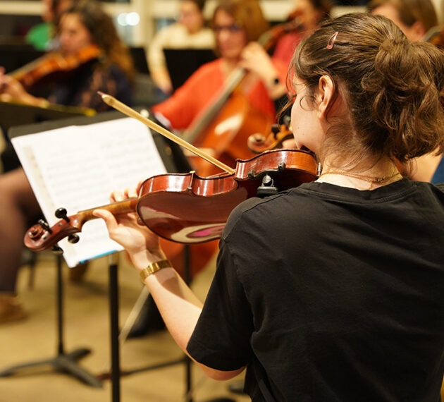 Jeune fille de dos qui joue du violon face à un pupitre.