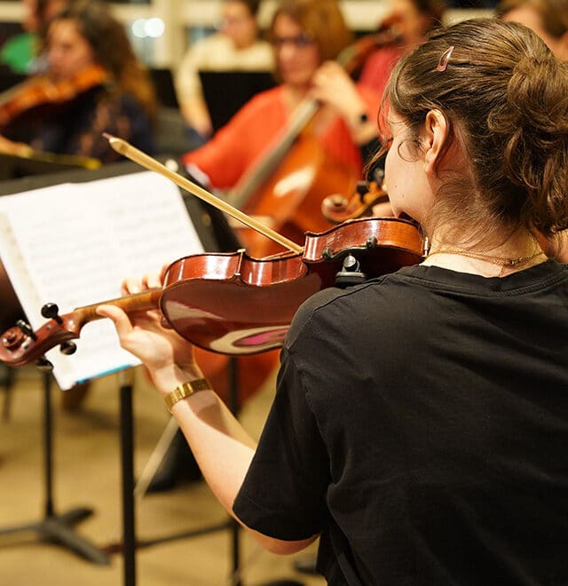 Jeune fille de dos qui joue du violon face à un pupitre.